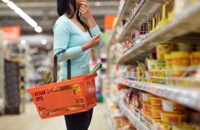 woman holding shopping basket looking at products in supermarket