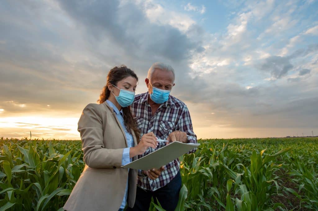 Business woman and farmer signing papers in corn field