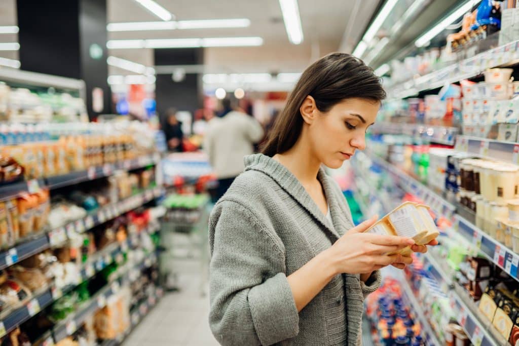 Young woman shopping in the supermarket grocery store.Reading ingredients,declaration or expiration date on a dairy product before buying it.Nutritional values of the food.Lactose intolerance