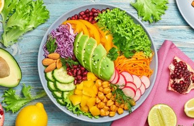 Buddha bowl salad with avocado, tomato, lettuce, cucumber, red cabbage, chickpeas, pomegranate. Paleo diet, healthy vegan and balanced food concept. Fresh rainbow mix green salad on wood, flat lay