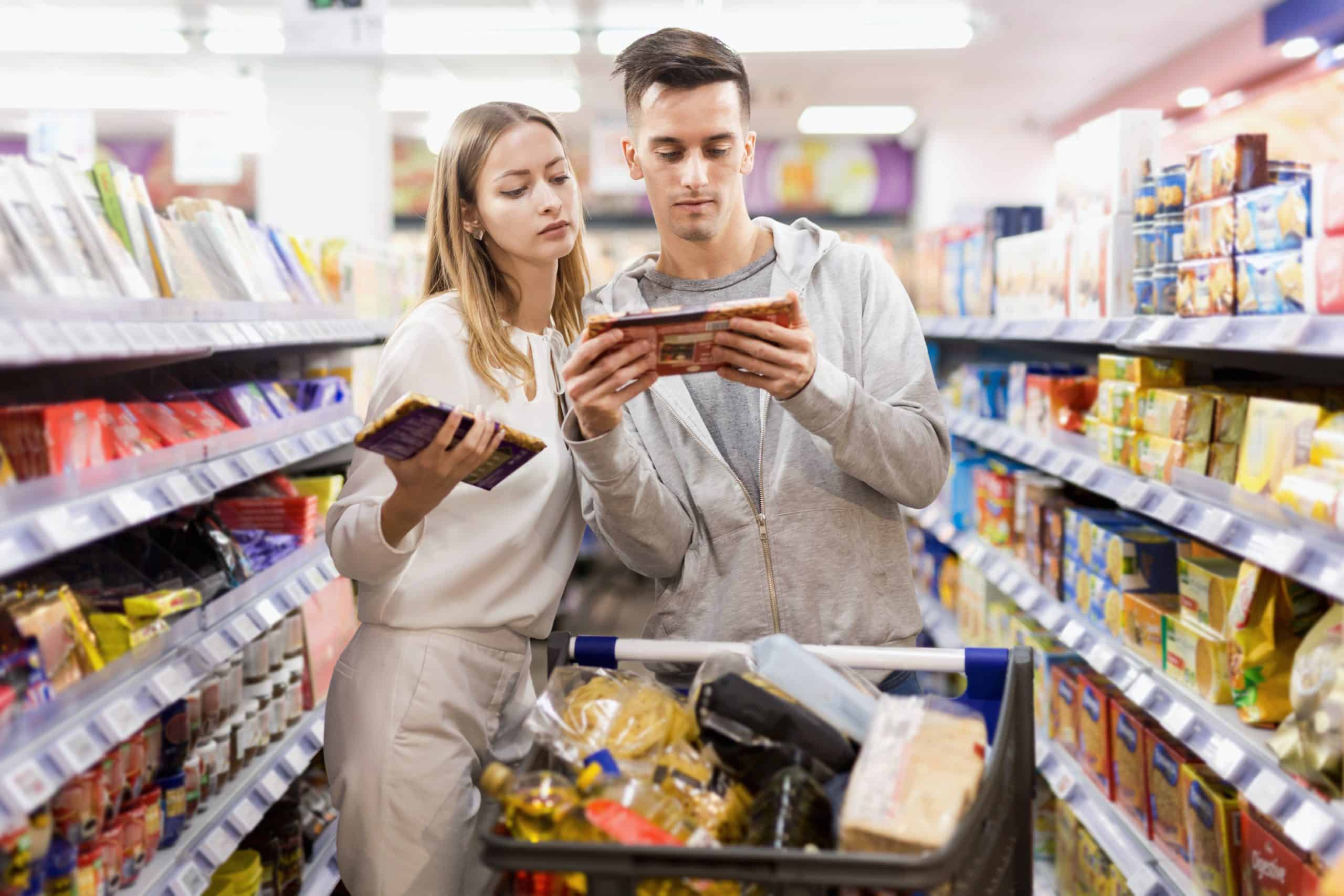 Young positive glad smiling couple of customers choosing chocolate in food department of supermarket