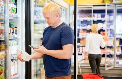 Mature man scanning barcode on product through mobile phone in grocery store